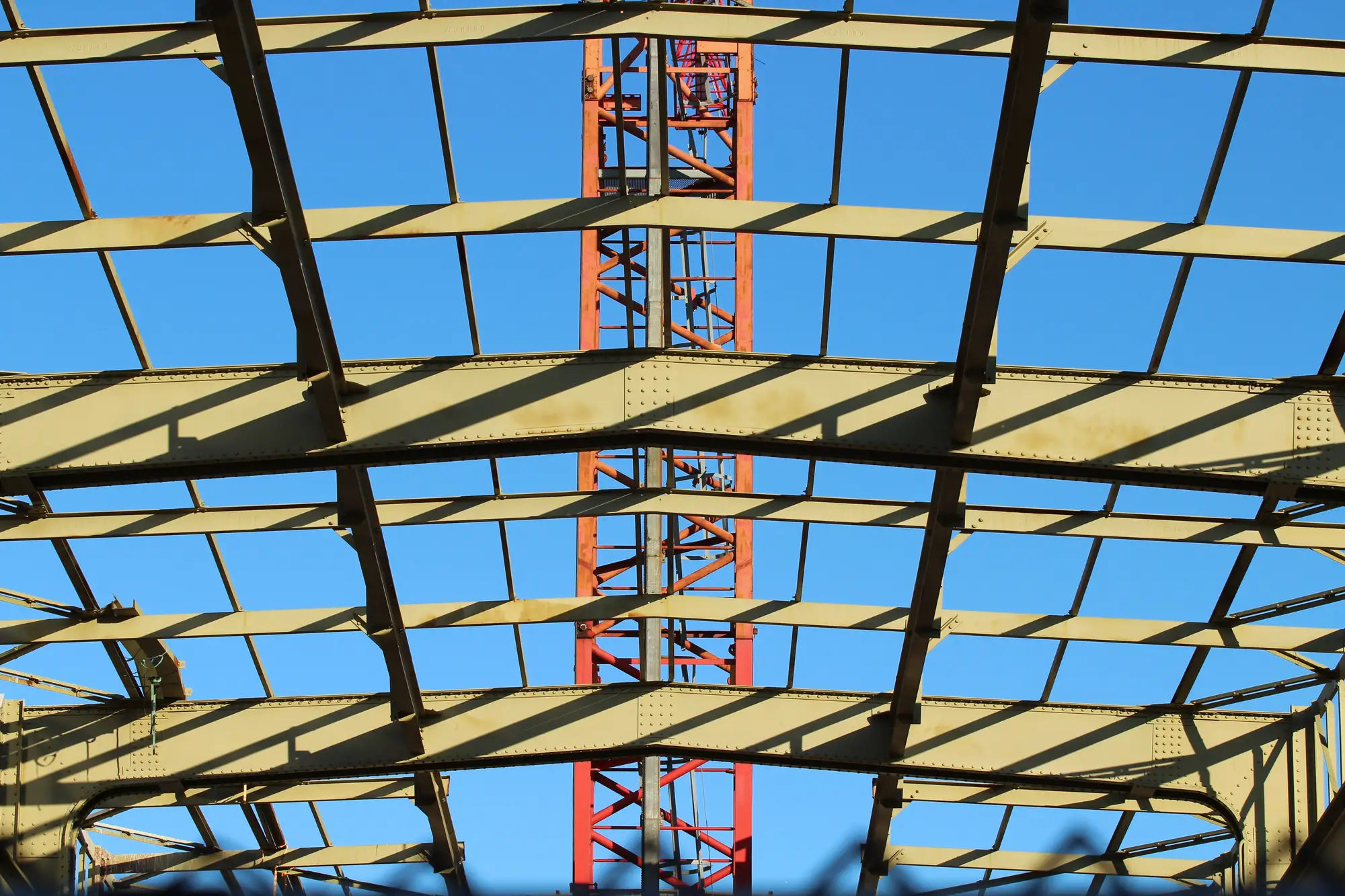 Steel roof trusses of a new building against a blue sky, a crane mast behind